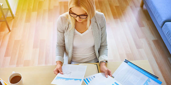 Young businesswoman working from home office with financial documents, notebook and laptop.