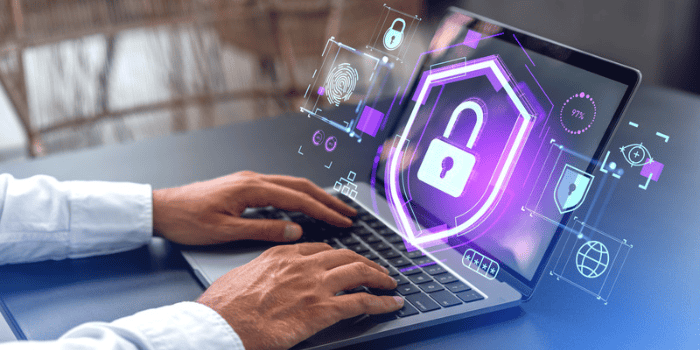 Hands of businessman using laptop with double exposure of futuristic data interface with padlock, fingerprint and shield at office table.